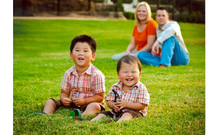 Two smiling adopted children sitting in front of their parents on a lawn